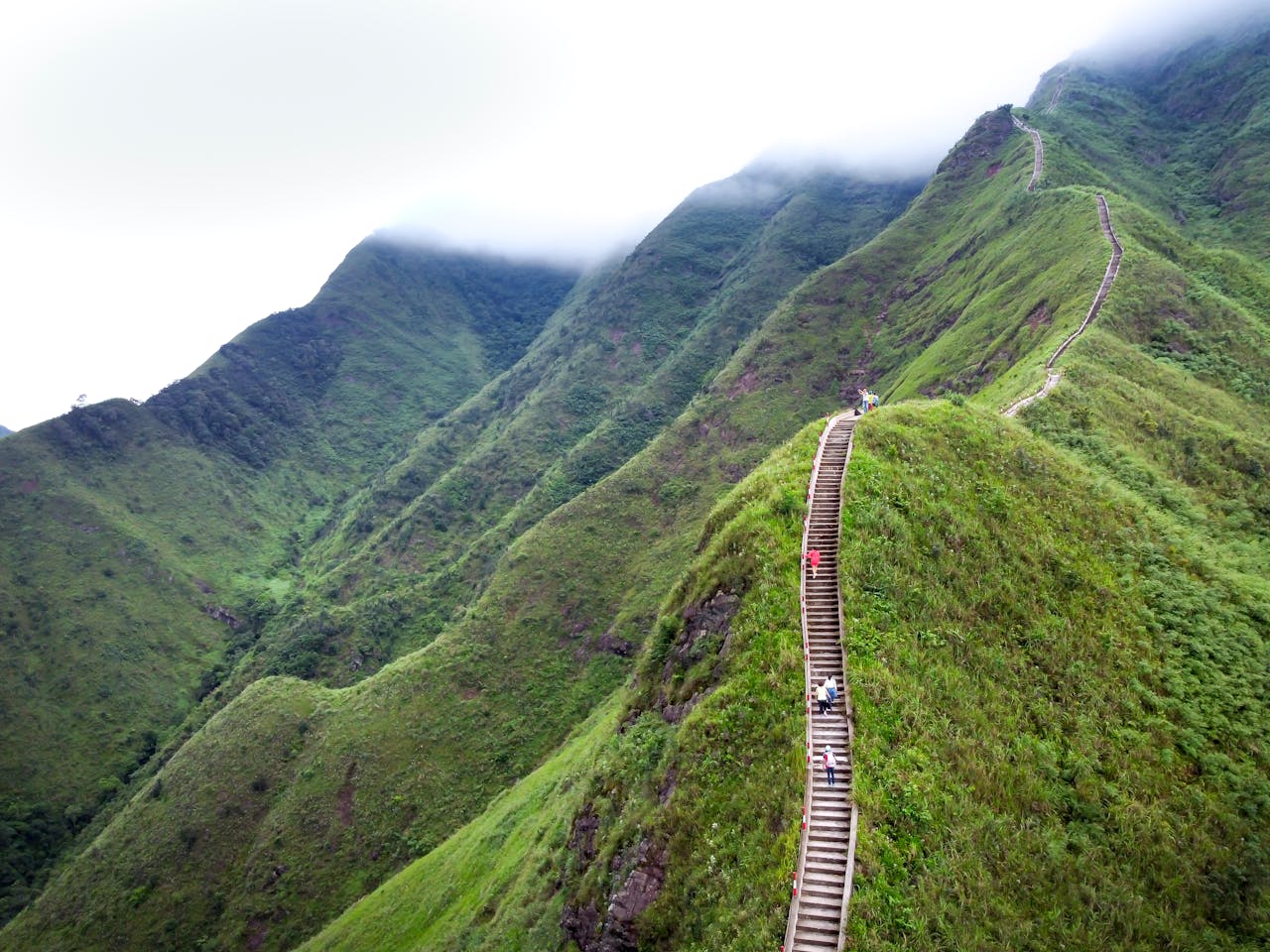 Aerial view of a stunning staircase winding through verdant mountains under a cloudy sky.